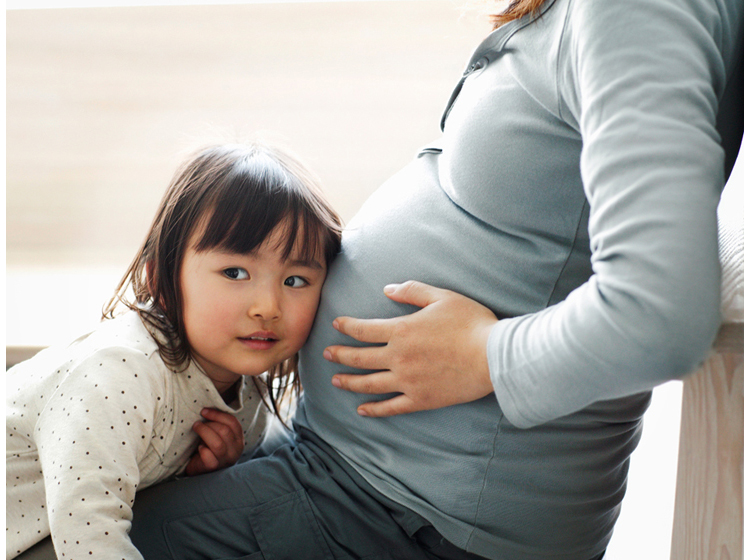 little girl holds her ear up next to her mum's pregnant belly