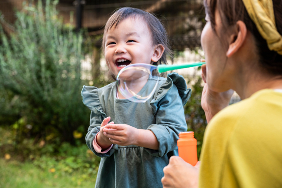 A toddler laughing while her mother blows bubbles